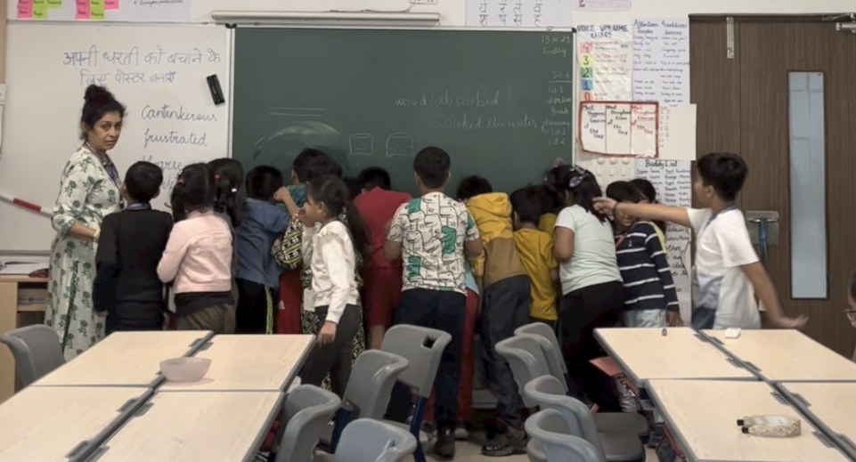 Children crowding at the blackboard, peeping behind it to find where the water went