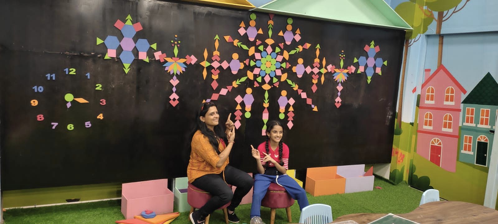 A parent and child at the magnetic wall, a large pattern of coloured shapes and numbers built on it